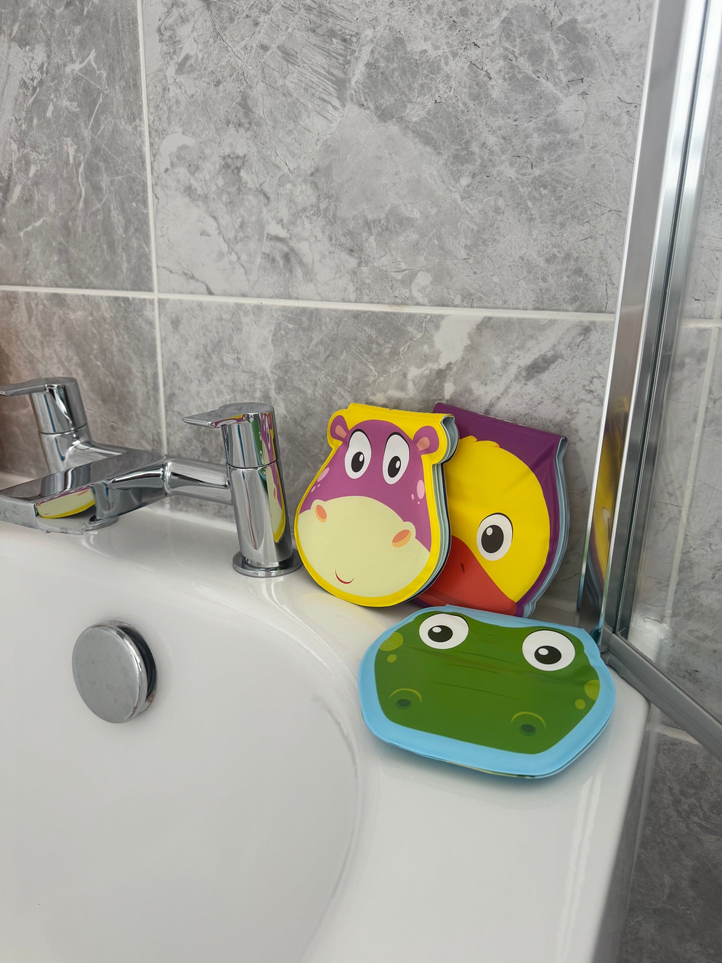 Colorful bath toys shaped like animals on a bathtub ledge with tiled wall background