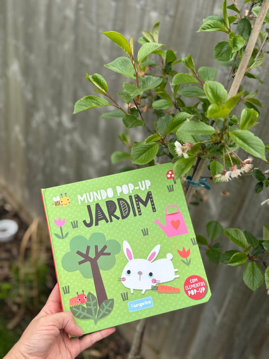 Children's pop-up book titled 'Mundo Pop-Up Jardim' held in front of a plant.