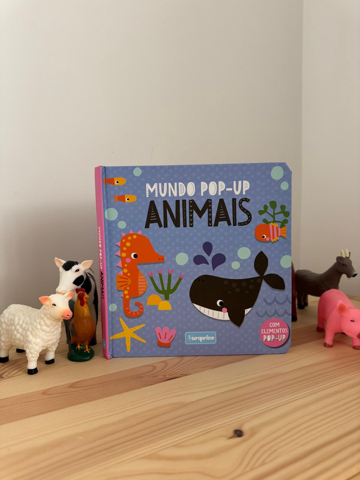 Children's book titled 'Mundo Pop-up Animais' with animal figurines on a wooden surface.