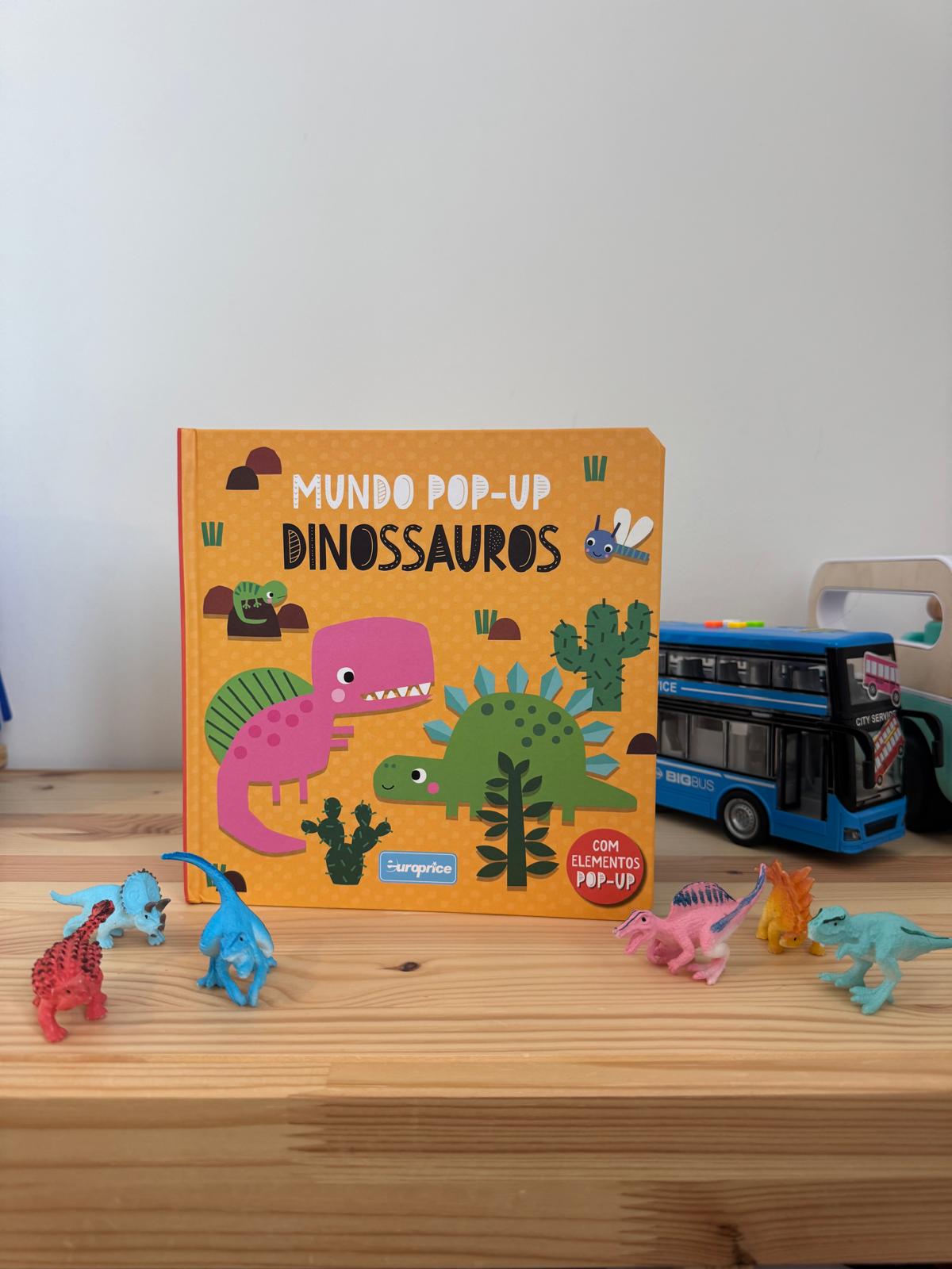 Children's pop-up book titled 'Dinossauros' with toy dinosaurs on a wooden surface.