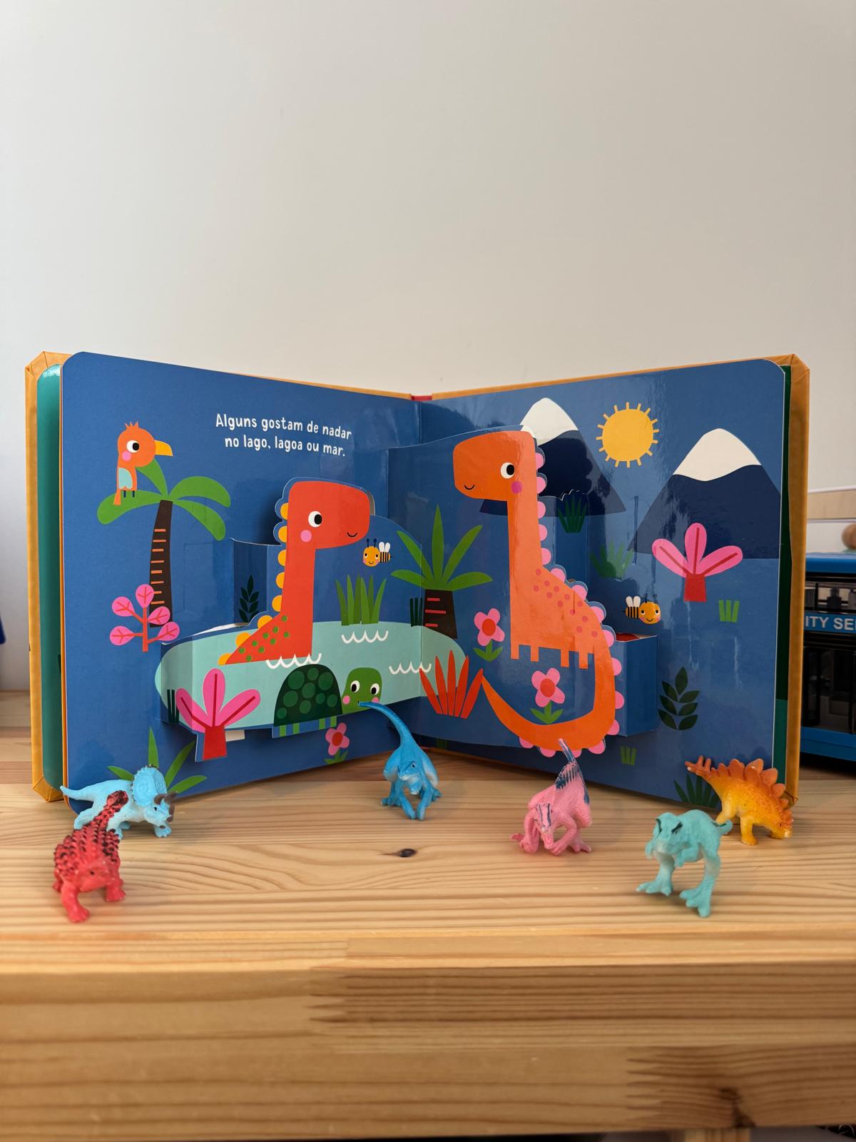 Children's book with dinosaur illustrations and small toy dinosaurs on a wooden surface